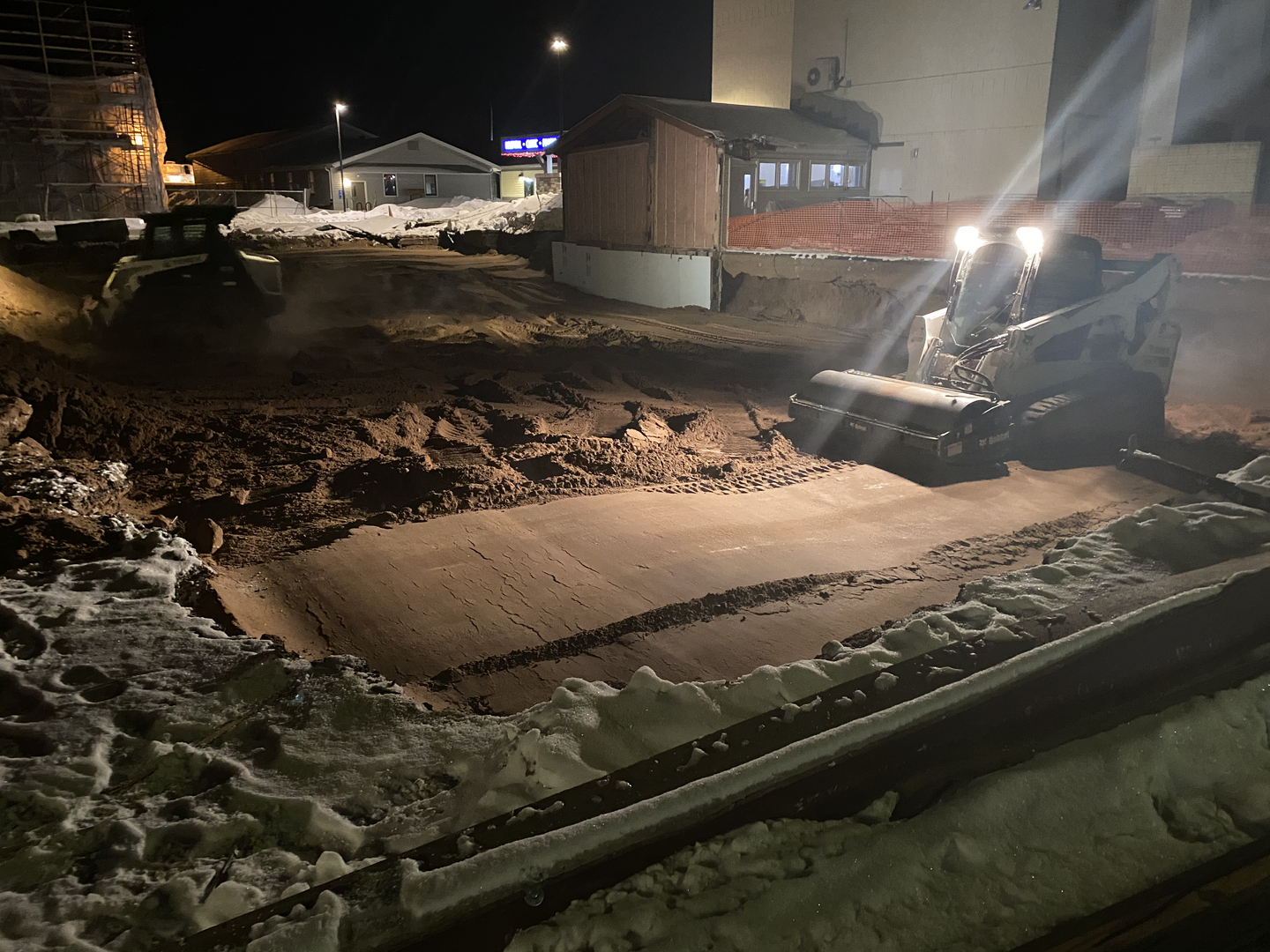 Bobcat skid-steer grading clinic demolition site at night