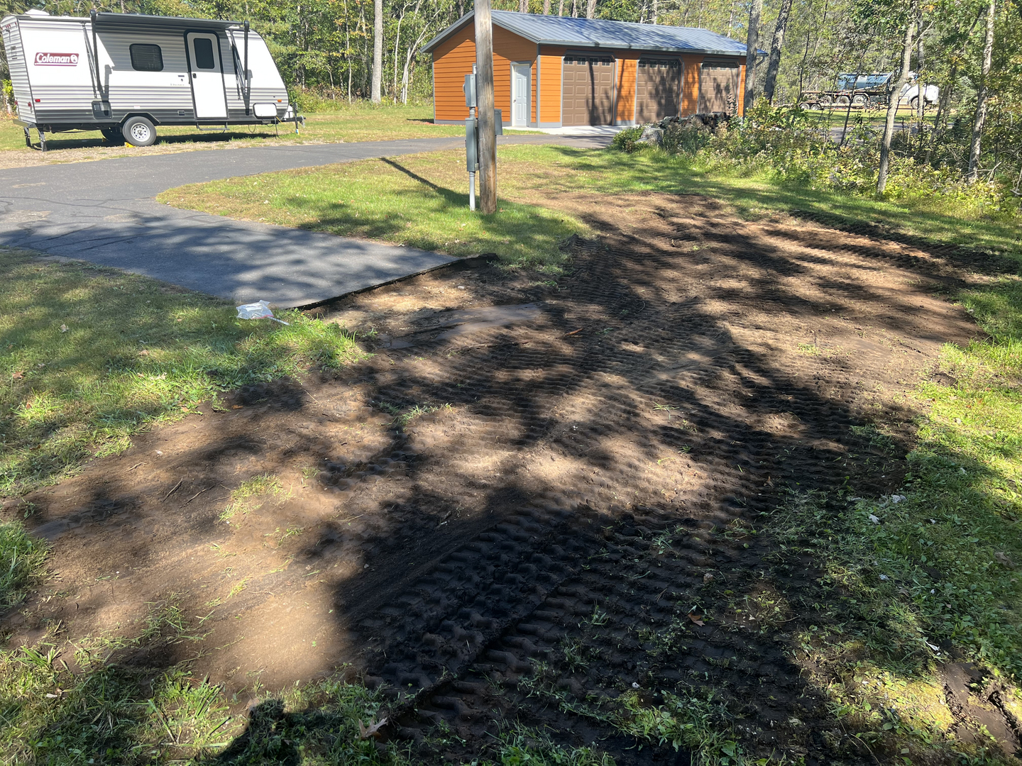 Skid-steer grading dirt near garage and camper